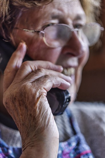 Laughing senior citizen with smock talking on the phone at home in her living room, Cologne, North Rhine-Westphalia, Germany, Europe