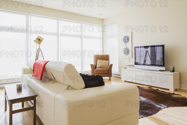 White leather sofa and brown sitting chair in living room inside a renovated ground floor apartment in an old residential cottage style home, Quebec, Canada, North America