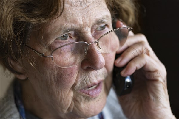 Senior citizen looks serious, frightened while talking on the phone in her living room, Cologne, North Rhine-Westphalia, Germany, Europe