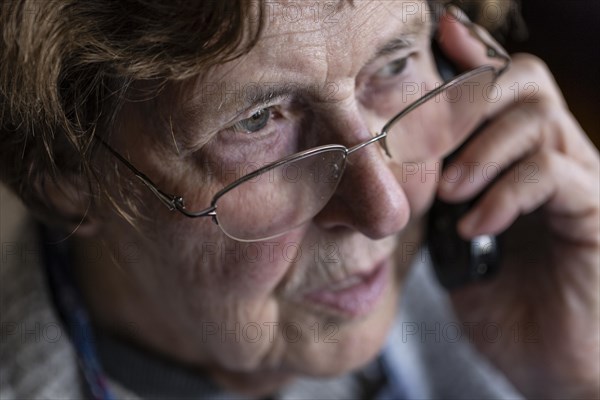 Senior citizen looks serious, frightened while talking on the phone in her living room, Cologne, North Rhine-Westphalia, Germany, Europe