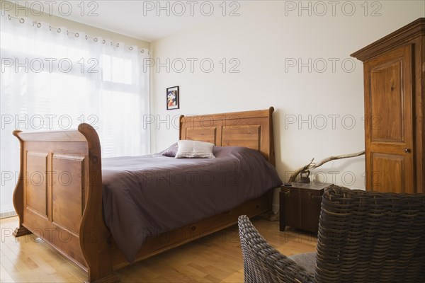 Antique wooden queen size sleigh bed in master bedroom inside a renovated ground floor apartment in an old residential cottage style home, Quebec, Canada, North America