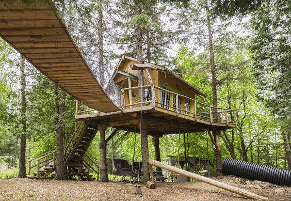 Children's playground and fancy tree house with half log stairs and elevated walkway in residential backyard in spring, Quebec, Canada, North America