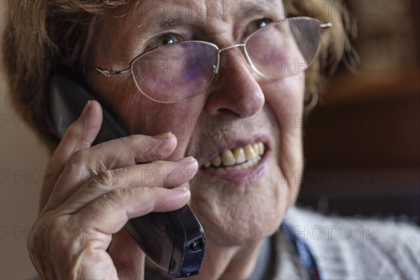 Senior citizen looks serious, frightened while talking on the phone in her living room, Cologne, North Rhine-Westphalia, Germany, Europe