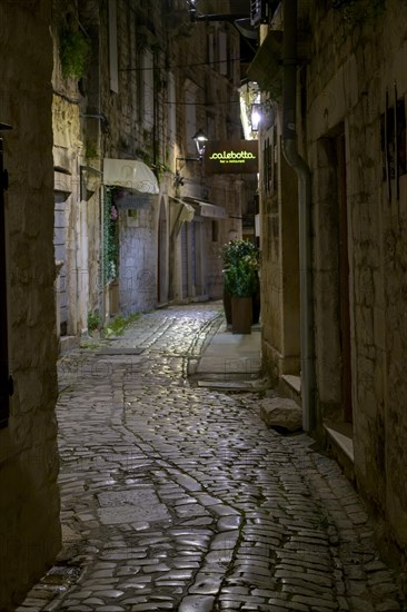 An illuminated alleyway with cobblestones and historic buildings at night, Trogir, Dalmatia, Croatia, Europe