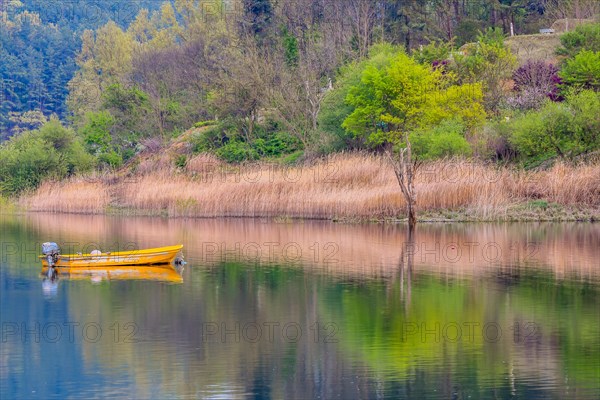 Small yellow metal fishing boat with small engine mount floating peacefully on a lake in South Korea