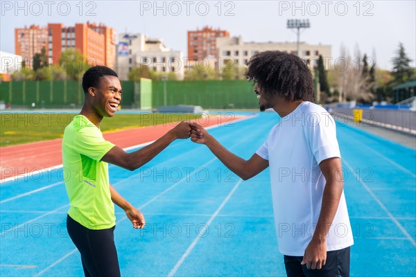Two happy and smiling young african runners fist bumping in greeting before training on an outdoor track
