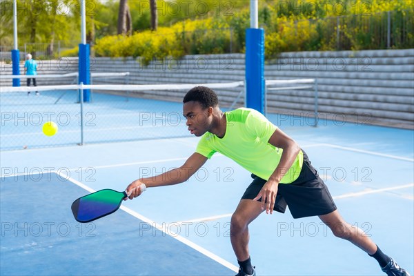 Concentrated african american young fit man playing pickleball in an outdoor court