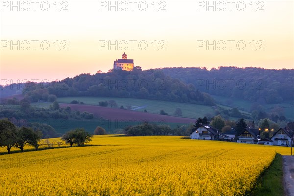 Landscape at sunrise. Beautiful morning landscape with fresh yellow rape fields in spring. Small castle in the yellow fields on a hill. Historic Ronneburg Castle in the middle of nature, Ronneburg, Hesse, Germany, Europe