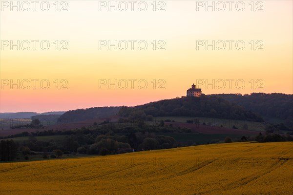 Landscape at sunrise. Beautiful morning landscape with fresh yellow rape fields in spring. Small castle in the yellow fields on a hill. Historic Ronneburg Castle in the middle of nature, Ronneburg, Hesse, Germany, Europe