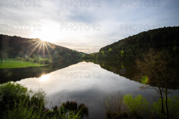 A lake in a landscape shot. A sunset and the natural surroundings are reflected in the water of the reservoir. Marbach reservoir, Odenwald, Hesse