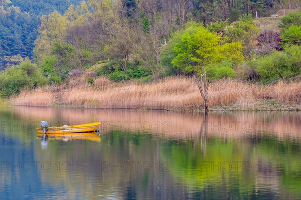 Small yellow metal fishing boat with small engine mount floating peacefully on a lake in South Korea