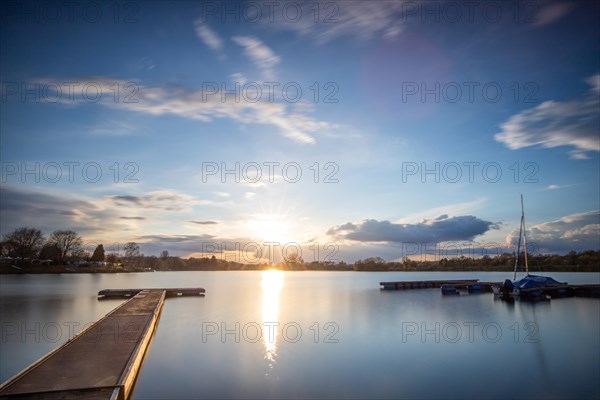 View from the shore into the distance and a sunset on the lake. The surroundings and the marvellous sky are reflected in the water. A great landscape shot Dutenhofener See, Hesse Germany