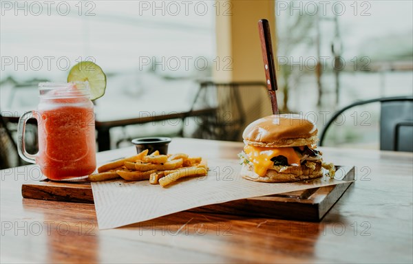 Delicious Hamburger with fries and strawberry cocktail served on a wooden table. Hamburger with strawberry cocktail served on table