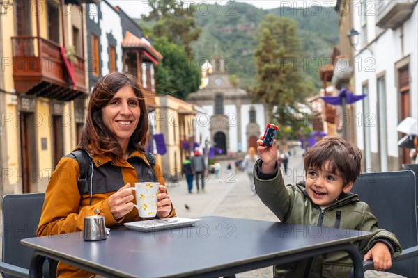 A woman and a child are sitting at a table in a city street, smiling and enjoying their time together