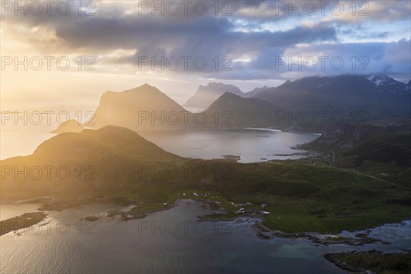 Landscape on the Lofoten Islands. View from the mountain Offersoykammen to the sea, the mountains Veggen, Mannen, Himmeltindan and Hogskolmen as well as the beaches of Haukland (Hauklandstranda) and Vik (Vik Beach) . At night at the time of the midnight sun. Clouds in the sky, sunlight from the side. Vestvagoya, Lofoten, Norway, Europe