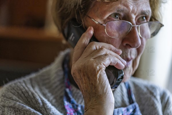 Senior citizen looks serious, frightened while talking on the phone in her living room, Cologne, North Rhine-Westphalia, Germany, Europe