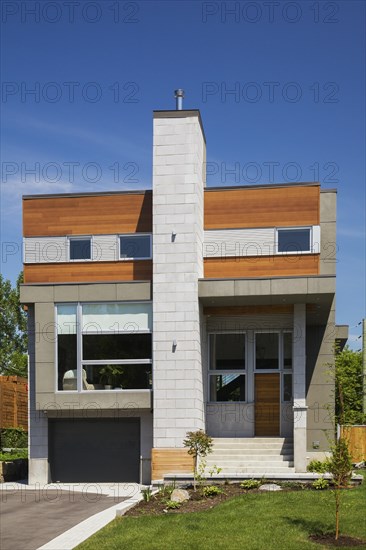 Two story grey and charcoal stone with cedar wood siding modern cube style home facade in summer, Quebec, Canada, North America