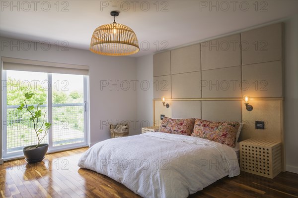 King size bed covered with white bedspread in bedroom with American walnut hardwood flooring on upstairs floor inside modern cube style home, Quebec, Canada, North America
