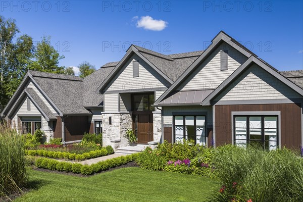 Contemporary natural stone and brown stained wood and cedar shingles clad luxurious bungalow style home facade in summer, Quebec, Canada, North America