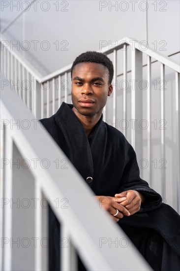 Vertical portrait of a handsome african american model with black warm clothes sitting on outdoor stairs