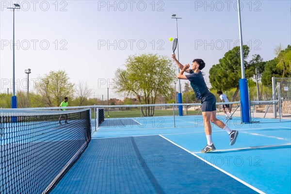 Full length photo of a young caucasian man jumping while playing pickleball in an outdoor facility