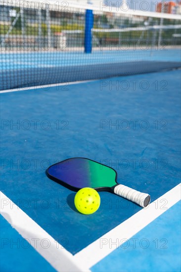 Vertical photo with copy space of a racket and yellow pickleball ball on a court