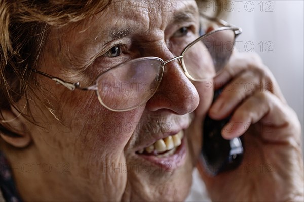 Laughing senior citizen talking on the phone at home in her living room, Cologne, North Rhine-Westphalia, Germany, Europe