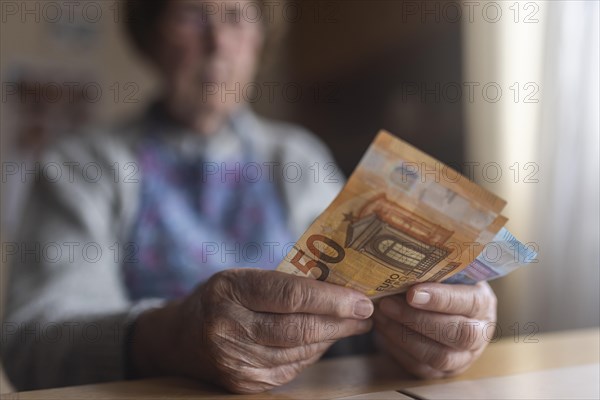 Senior citizen with wrinkled hands counts her money at home in her flat and holds banknotes in her hand, Cologne, North Rhine-Westphalia, Germany, Europe