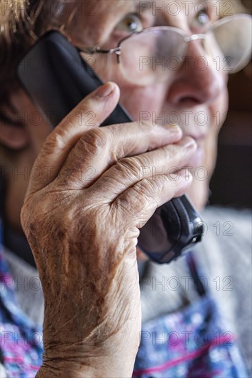 Senior citizen looks serious, frightened while talking on the phone in her living room, Cologne, North Rhine-Westphalia, Germany, Europe