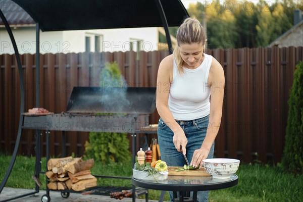 Mid adult woman makes vegetable salad while waiting for grill become hot