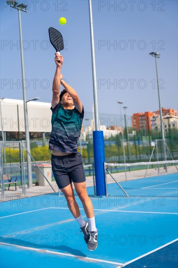 Vertical full length photo of a caucasian young sportive man jumping to reach the ball playing pickleball outdoors