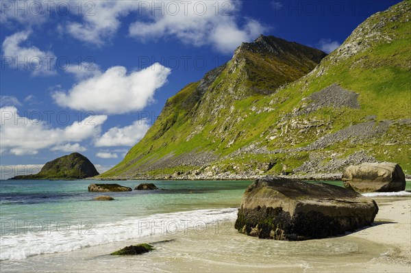 Landscape with sea at the sandy beach of Haukland (Hauklandstranda) with the mountain Veggen. Some rocks on the beach and in the sea. Blue sky, some clouds. Early summer. Haukland Beach, Haukland, Vestvagoya, Lofoten, Norway, Europe