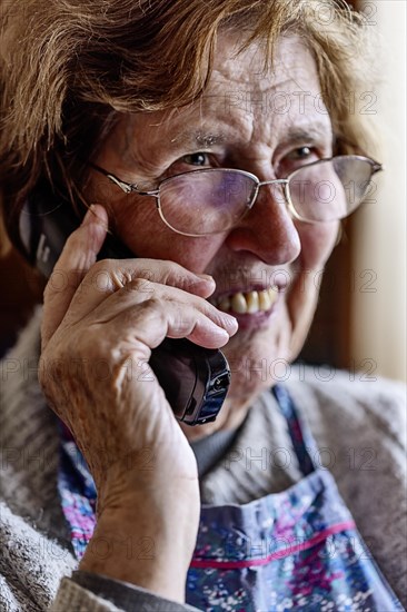 Laughing senior citizen with smock talking on the phone at home in her living room, Cologne, North Rhine-Westphalia, Germany, Europe