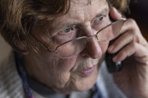 Senior citizen looks serious, frightened while talking on the phone in her living room, Cologne, North Rhine-Westphalia, Germany, Europe