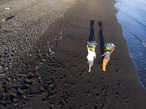 2 woman carry the freshly caught fish in the morning over the black lava beach of Amed, Karangasem district, Bali, Indonesia, Asia