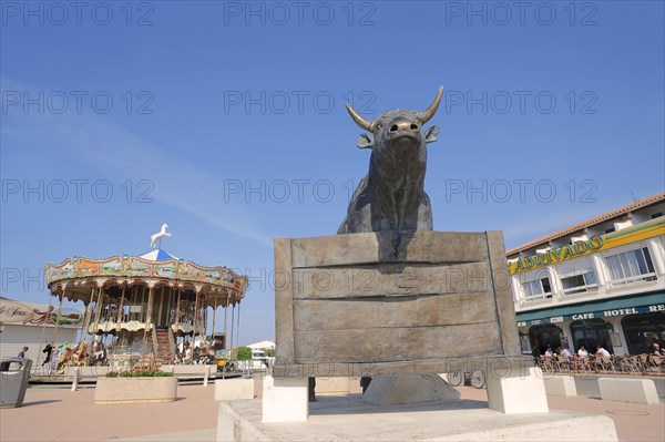 Statue of a Camargue bull and carousel, Les Saintes-Maries-de-la-Mer, Camargue, Bouches-du-Rhone, Provence-Alpes-Cote d'Azure, South of France, France, Europe