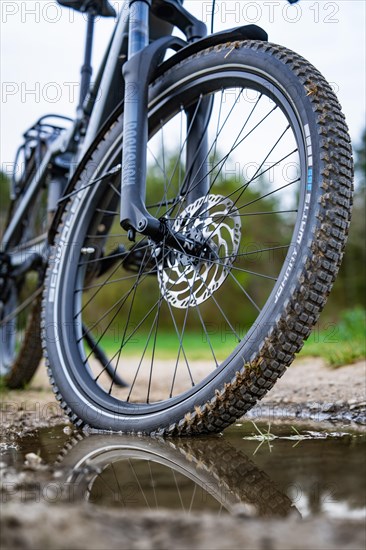 Close-up of a bicycle tyre in front of a puddle with reflections, spring, e-bike forest bike, Gechingen, Black Forest, Germany, Europe