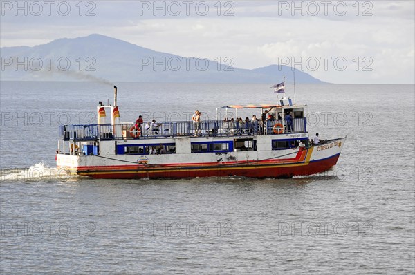 Lake Nicaragua, behind the island of Ometepe, ferry with passengers on the open sea, waving flag and a cloudy sky in the background, Nicaragua, Central America, Central America