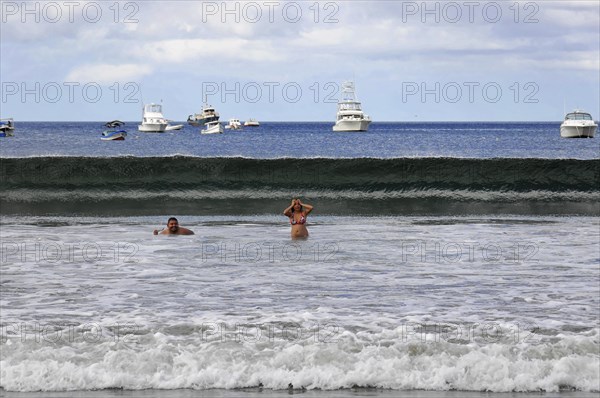 San Juan del Sur, Nicaragua, swimmers in the water in front of a big wave, boats and blue sky in the background, Central America, Central America