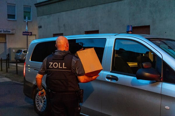 Customs officer at work, carrying cardboard to the official vehicle at dusk, The Cologne police led a raid against illegal gambling on Friday evening. Around 200 investigators from the police, customs, tax investigation department, public order office, tax office, foreigners authority and gas office were out on the streets of Cologne on Friday evening. They search 25 properties where there are indications that illegal gambling is taking place. And they make a find