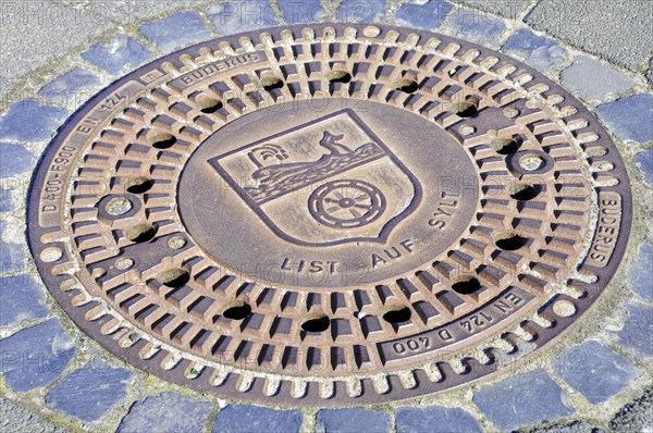 List, A manhole cover with engraved coat of arms and lettering, surrounded by paving stones, Sylt, North Frisian Island, Schleswig-Holstein, Germany, Europe