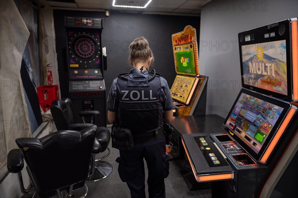Customs officer looks at slot machines and surveillance equipment in a dark room, The Cologne police led a raid against illegal gambling on Friday evening. Around 200 investigators from the police, customs, tax investigation department, public order office, tax office, foreigners authority and public catering office were out on the streets of Cologne on Friday evening. They search 25 properties where there are indications that illegal gambling is taking place. And they make a find