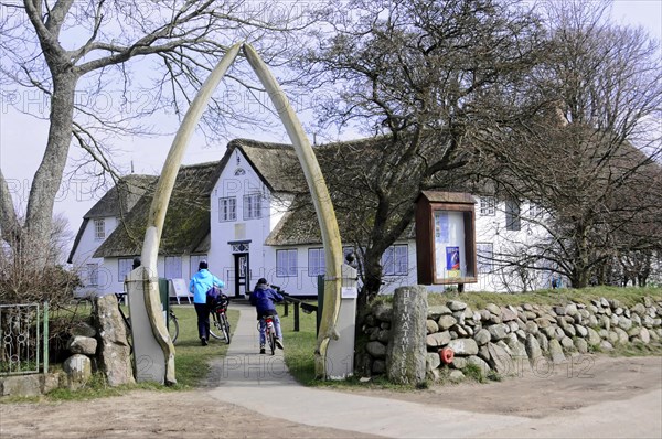 Sylt, North Frisian Island, Schleswig Holstein, Cyclists ride through an archway on a pebble path past historic houses, Sylt, North Frisian Island, Schleswig Holstein, Germany, Europe