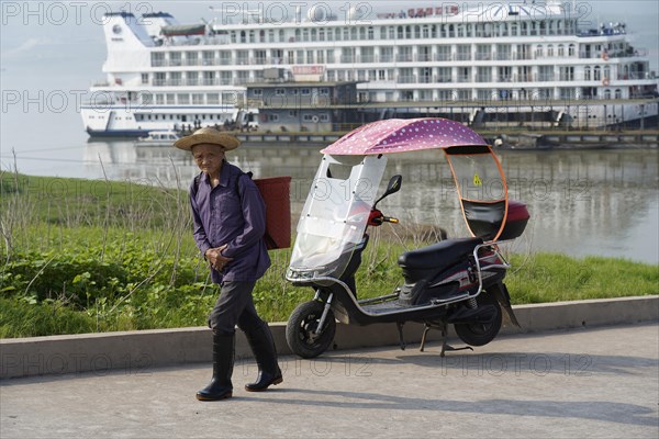 Cruise ship on the Yangtze River, A man walks next to an electric rickshaw, in the background a large cruise ship on the river, Yangtze River, Chongqing, Chongqing Province, China, Asia