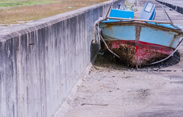 Front view of old dilapidated red, white and blue fishing boat with barnacles on bottom sitting on concrete next to wall in South Korea