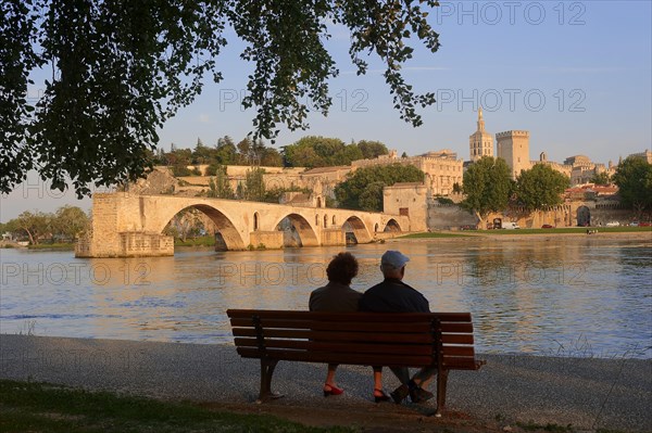 Couple on a park bench on the banks of the Rhone, Pont Saint Benezet bridge, Palais des Papes and Notre-Dame des Doms cathedral, Avignon, Vaucluse, Provence-Alpes-Cote d'Azur, Southern France, France, Europe
