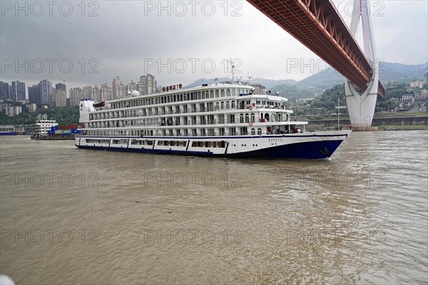 Chongqing, Chongqing Province, China, Cruise ship on a river under a large bridge on an overcast day, Chongqing, Chongqing, Chongqing Province, China, Asia