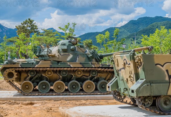 Side view of camouflaged tank used in Korean war behind armored landing vehicle on display in public park in Nonsan, South Korea, Asia