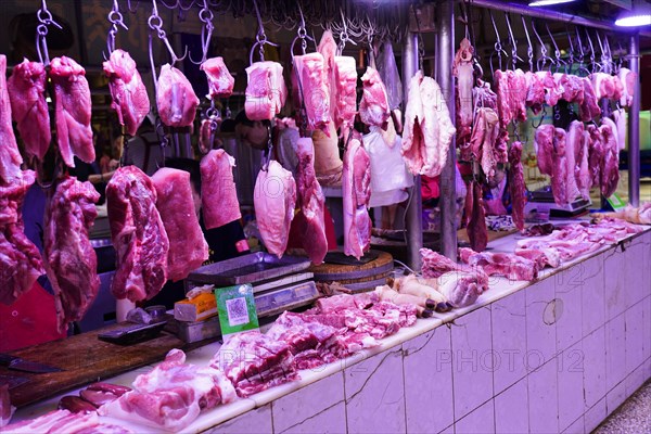 Chongqing, Chongqing Province, China, Pieces of meat hanging on hooks in an internally lit market stall, Chongqing, Chongqing Province, China, Asia