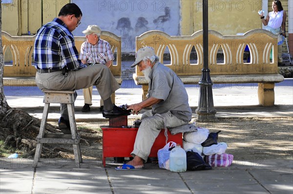 Leon, Nicaragua, A shoeshine boy serves a customer on the street under the shade of the trees, Central America, Central America